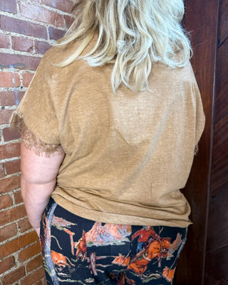 A person shown from the back wearing a tan short-sleeve top and dark patterned pants with orange and blue desert animal prints, standing against a brick wall and dark wood door.