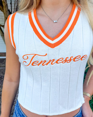 A close-up of a woman wearing a white ribbed knit V-neck tank top with orange and white striped trim and orange 'Tennessee' script across the chest.