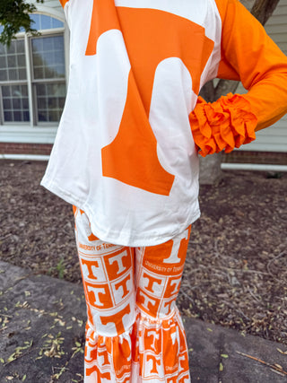 A person wearing a white and orange Tennessee Volunteers athletic set, featuring a long-sleeve top with a large orange 'T' on the back and matching ruffled flare pants with an orange and white 'T' pattern.