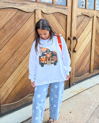 A woman stands in front of large wooden garage doors wearing a light blue sweatshirt with a cartoon truck graphic, light blue polka dot sweatpants, and sandals.