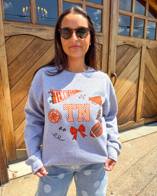A woman wearing a light heather gray sweatshirt with a Tennessee Titans graphic print, paired with light blue polka dot sweatpants, standing in front of a wooden garage door.