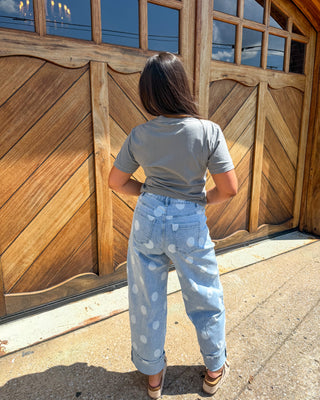 A person viewed from behind wearing a gray t-shirt and light blue wide-leg jeans with white polka dots, standing in front of a large wooden garage door.