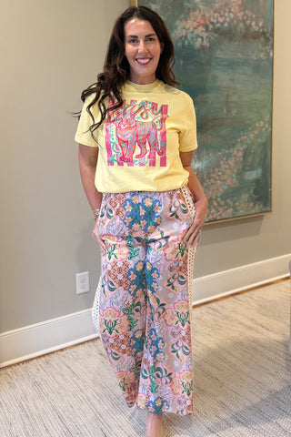 Woman wearing a yellow t-shirt with a colorful design and floral pants in an indoor setting.