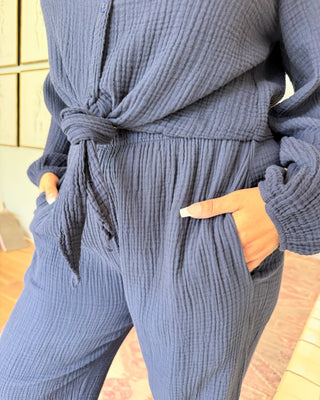 A person wearing a matching textured blue-gray long-sleeve top and pants set, with the top tied at the waist and hands in the side pockets.