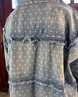 Close-up of the back of a light blue denim jacket with white polka dots and frayed horizontal seams.