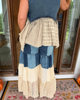 A person shown from the back wearing a patchwork denim and cream pant with a matching denim sleeveless top, standing on a floral rug in front of a glass door.