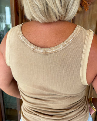 A close-up back view of a woman wearing a beige ribbed tank top with a scoop neckline trimmed with small gold sequins.