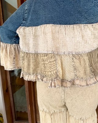 A close-up of a person wearing a patchwork-style ruffled top and matching beige ruffled pants, photographed indoors near a wooden door.