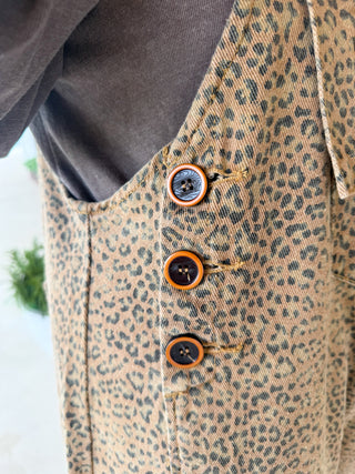 Close-up of a leopard-print garment with three decorative buttons featuring orange-rimmed black centers, worn over a dark gray top.